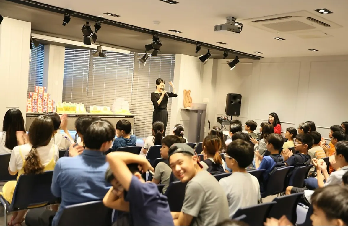 A teacher with a microphone hosting a prize quiz for a room of students