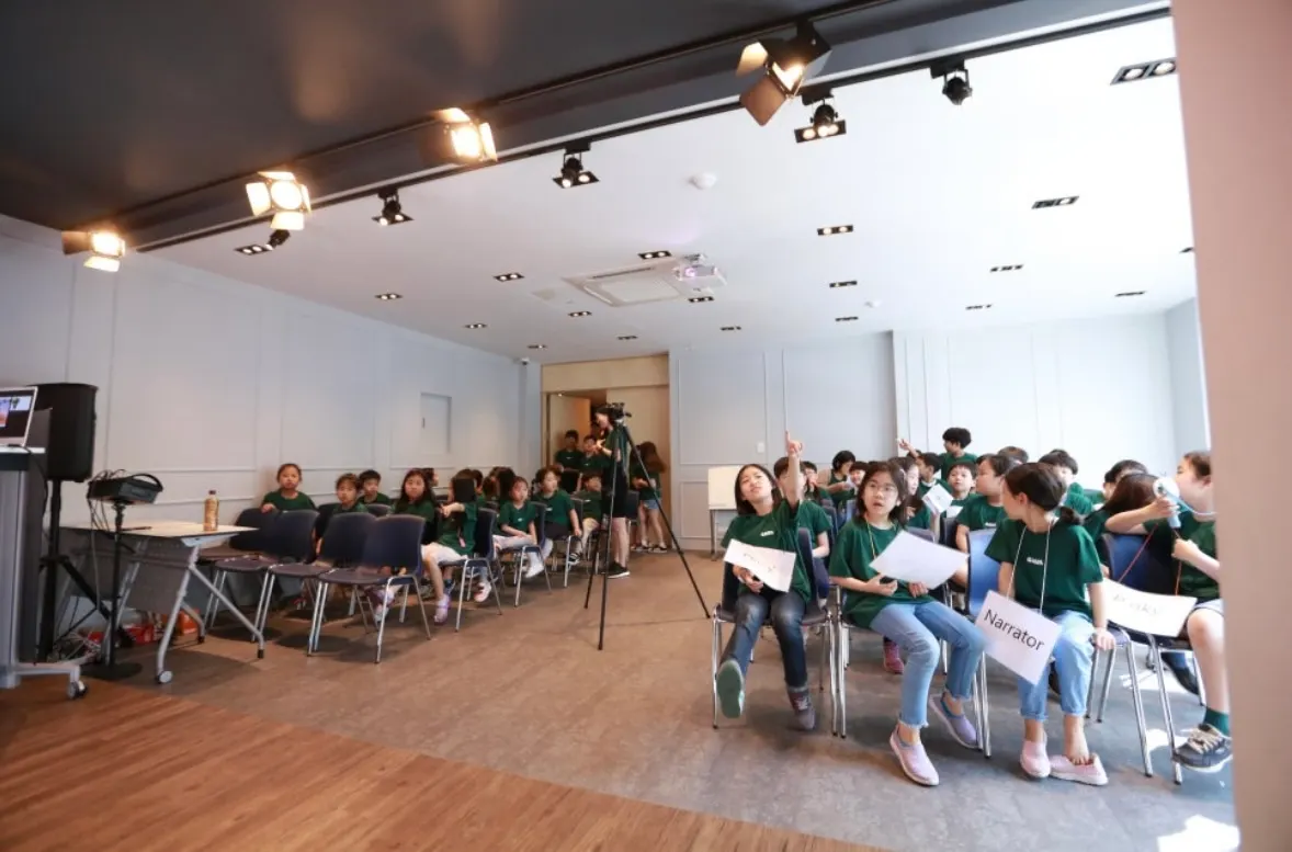 Students in GRAIL T-shirts holding role cards such as Narrator during a readers' theater session