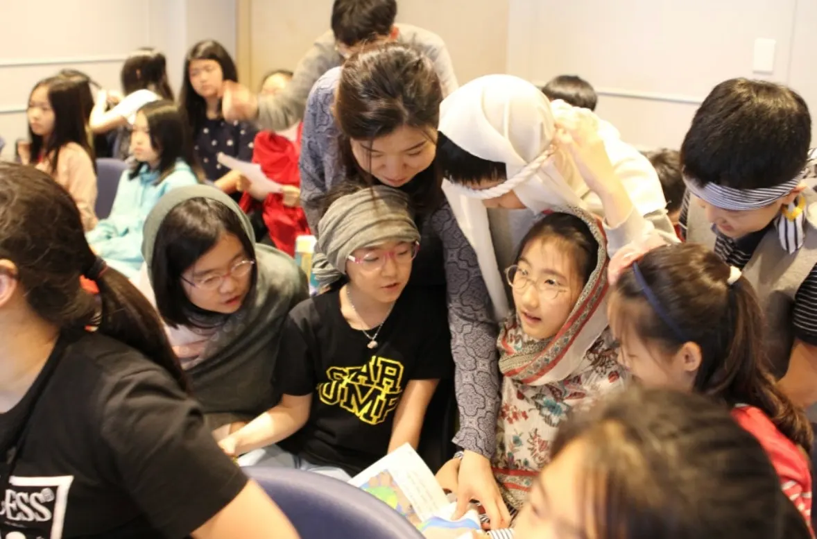 Students in costume headscarves reading a script together with a teacher