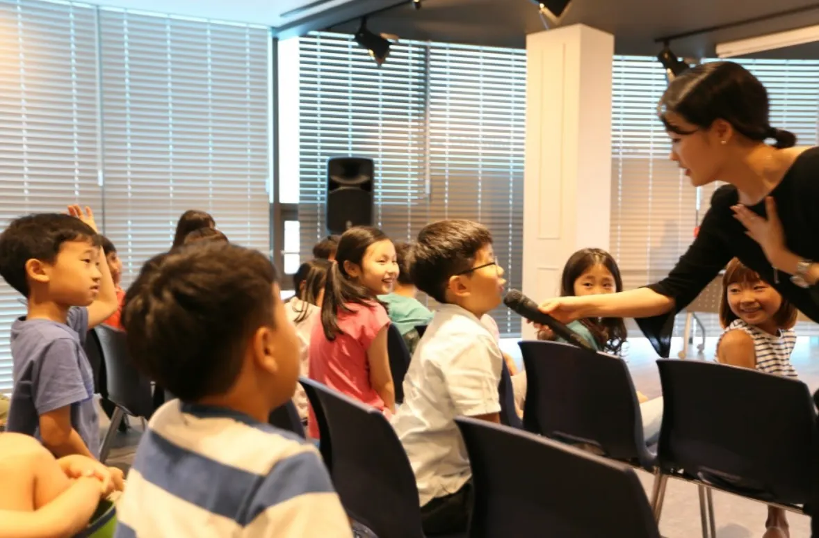 A teacher holding a microphone to a student during a class presentation