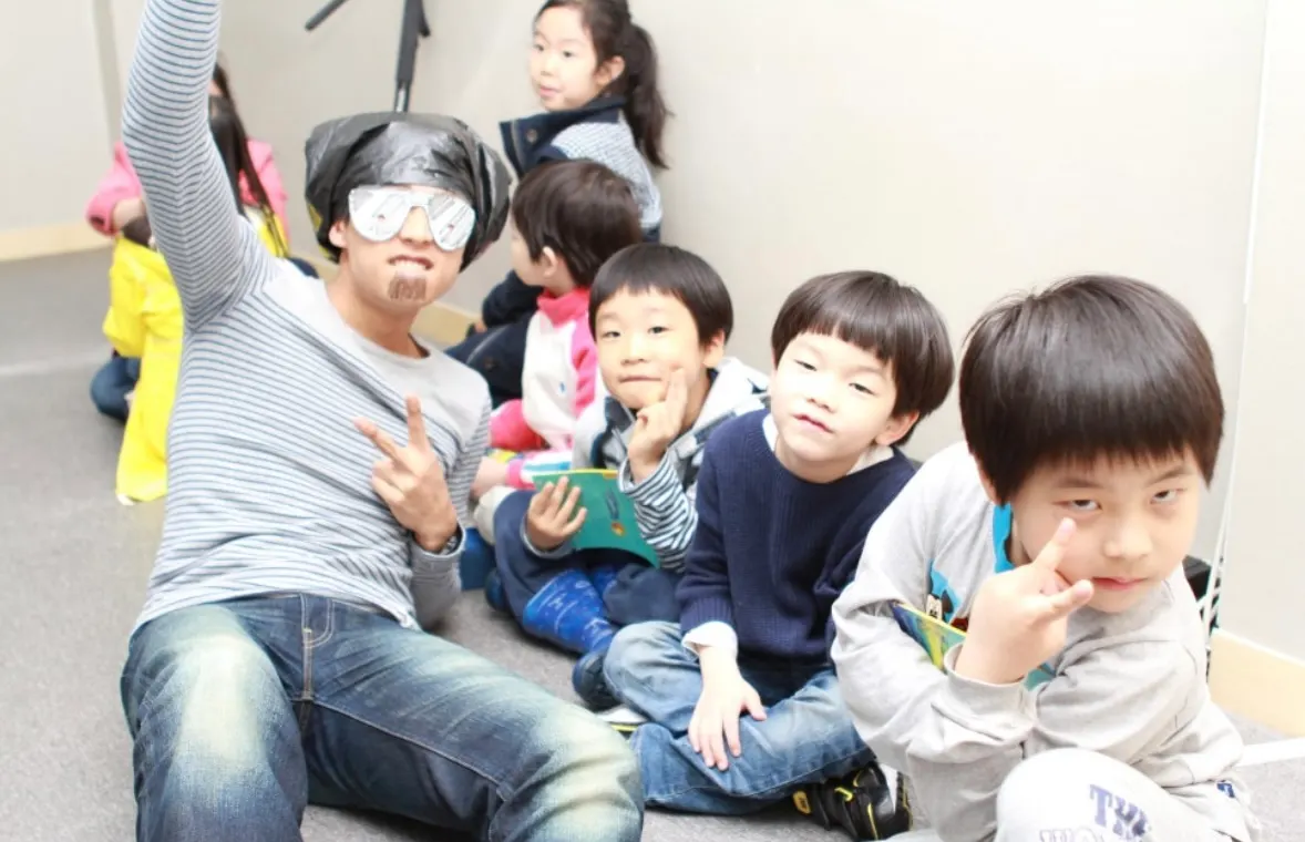 A teacher in a funny costume sitting on the floor with students during a story session