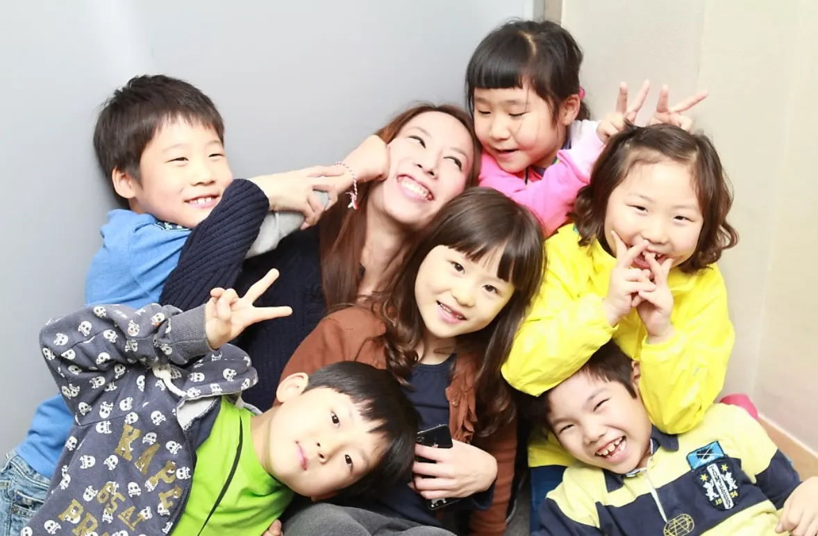 A smiling teacher surrounded by a group of laughing students